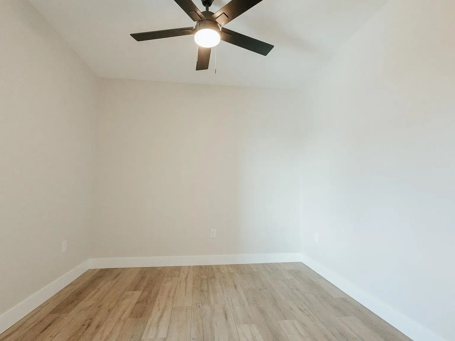 Empty room with Asher floor plan, light wood floors, white walls, and black ceiling fan with light.