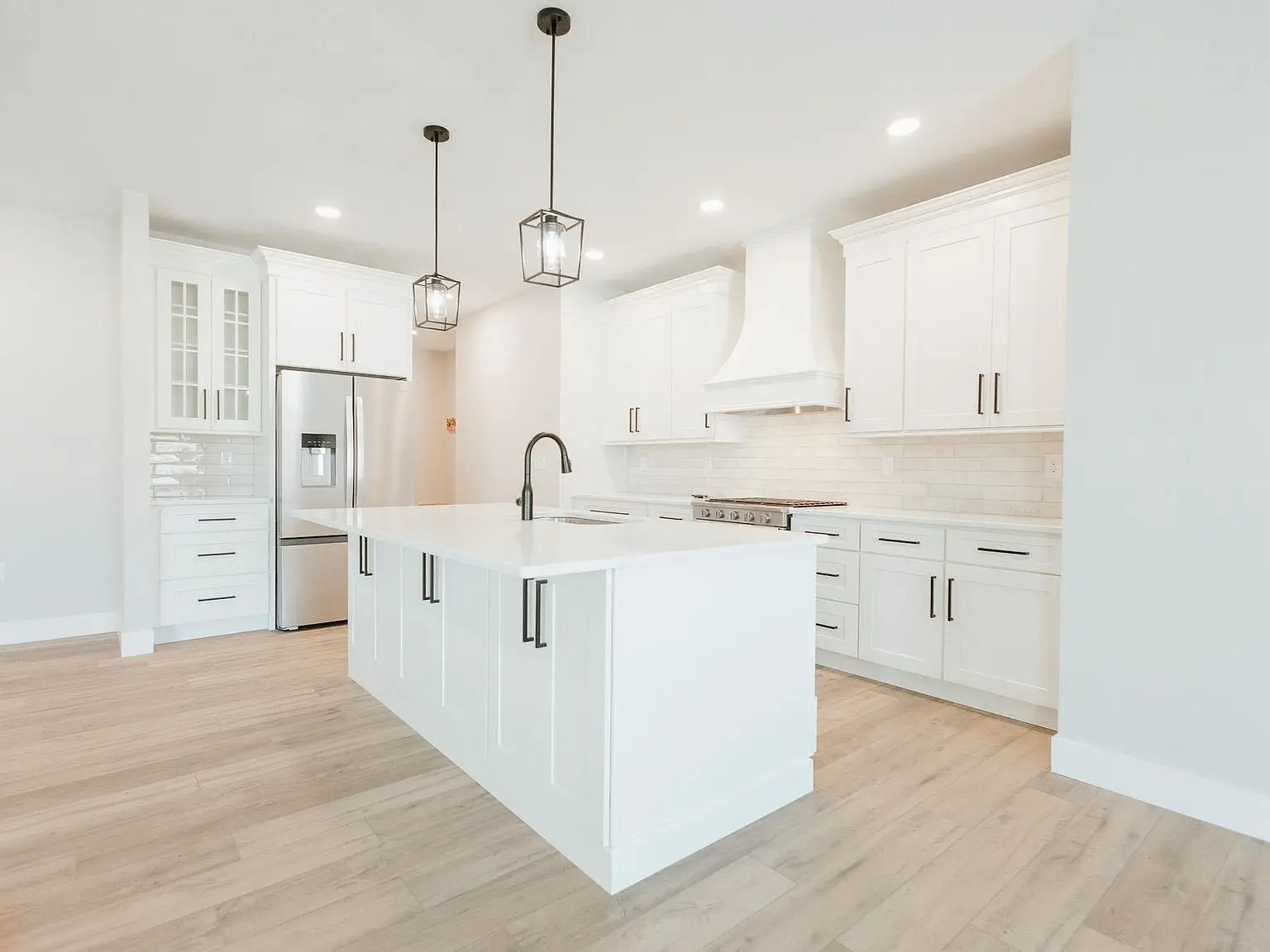 Modern white kitchen with island, Asher floor plan, pendant lights, and stainless appliances.