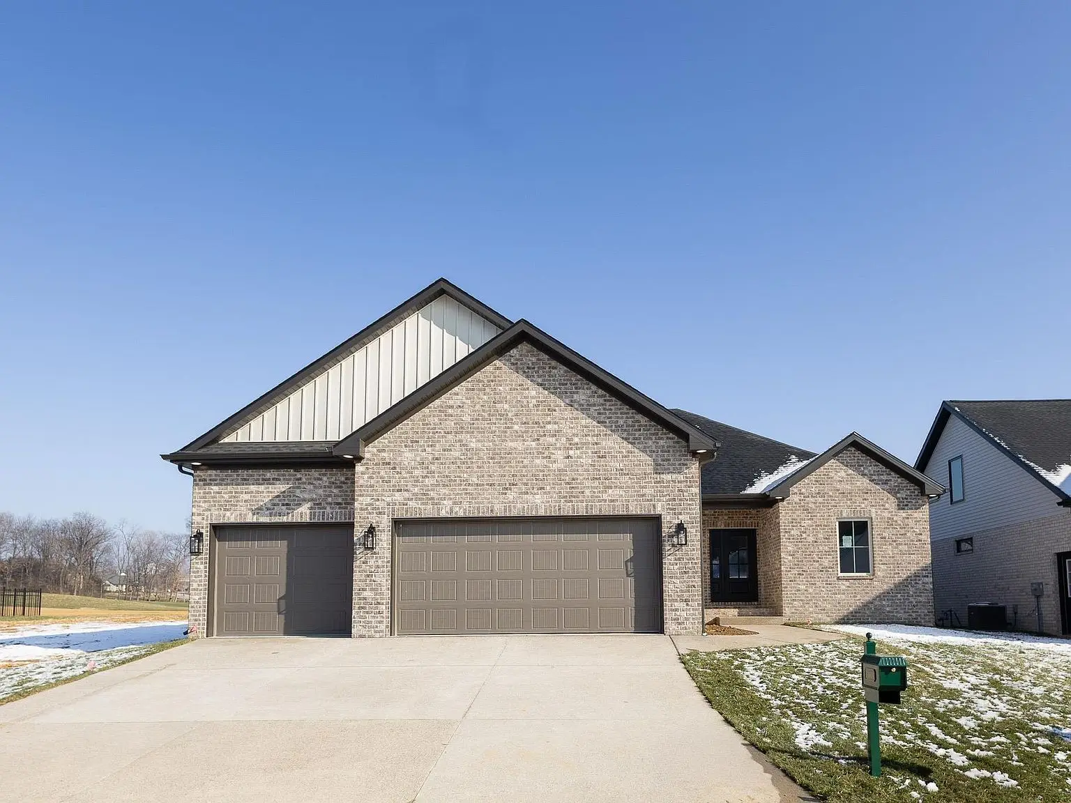Single-story Asher floor plan brick house with three-car garage and small patches of snow on lawn.