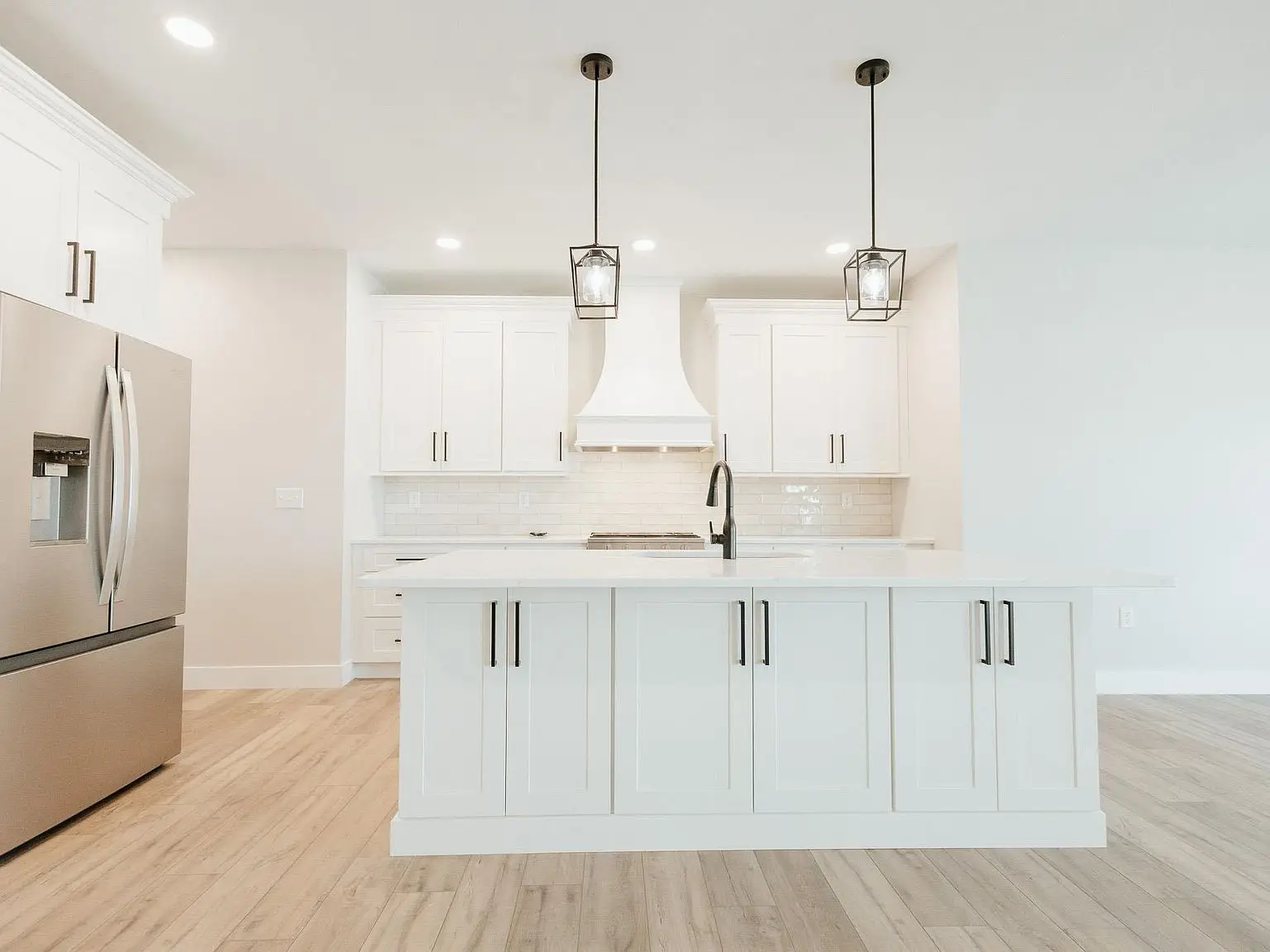 Modern Asher kitchen with white cabinets, pendant lights, large island, and stainless steel fridge.