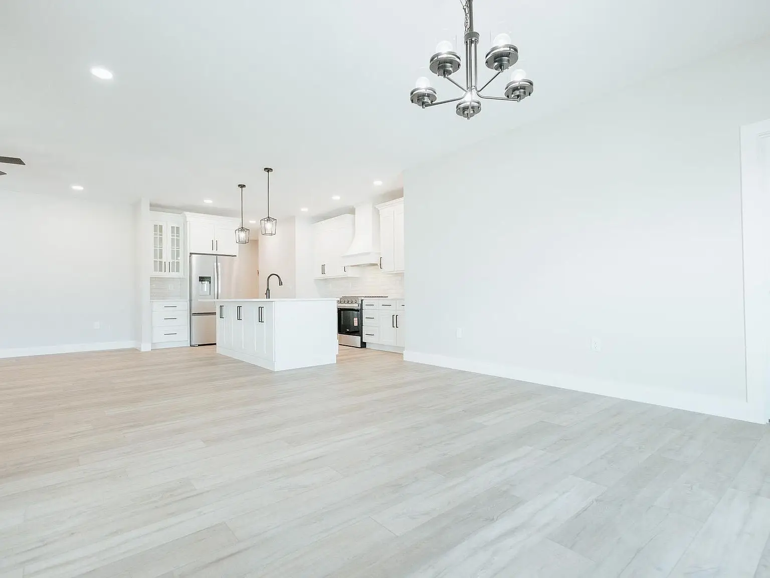 Bright, empty Asher floor plan kitchen and living area with light wood floors and white walls.