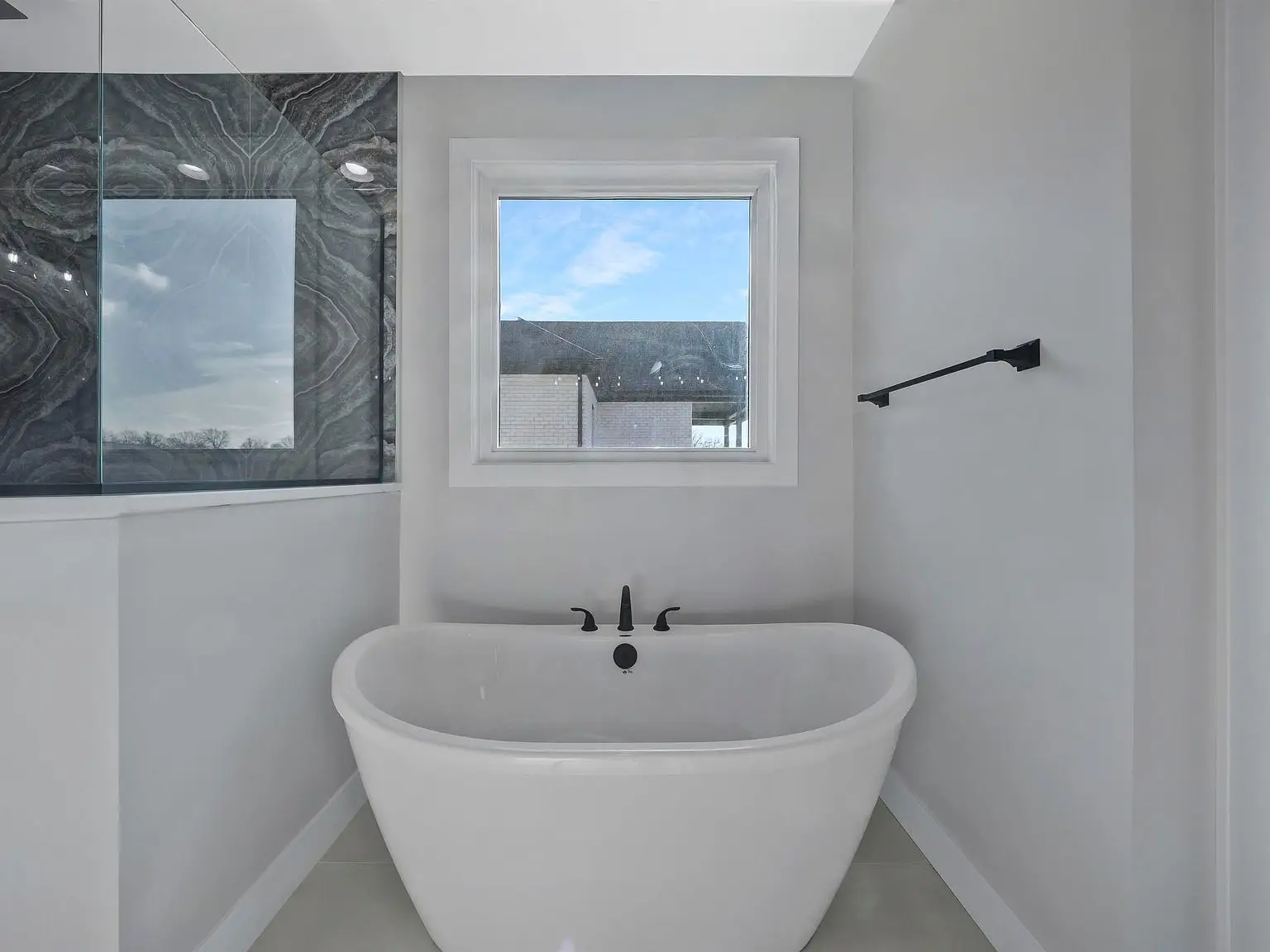 Freestanding white tub under window with black fixtures in modern Chris Brown Homes Ava bathroom.