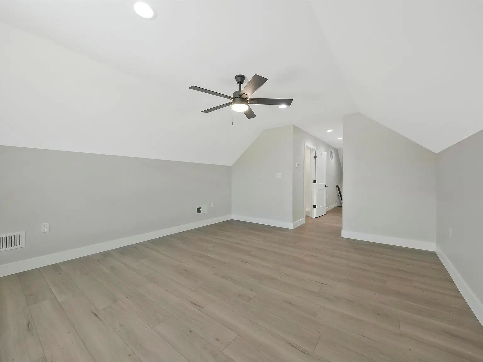 Empty attic room in the Ava floor plan features light wood flooring, white walls, and ceiling fan.