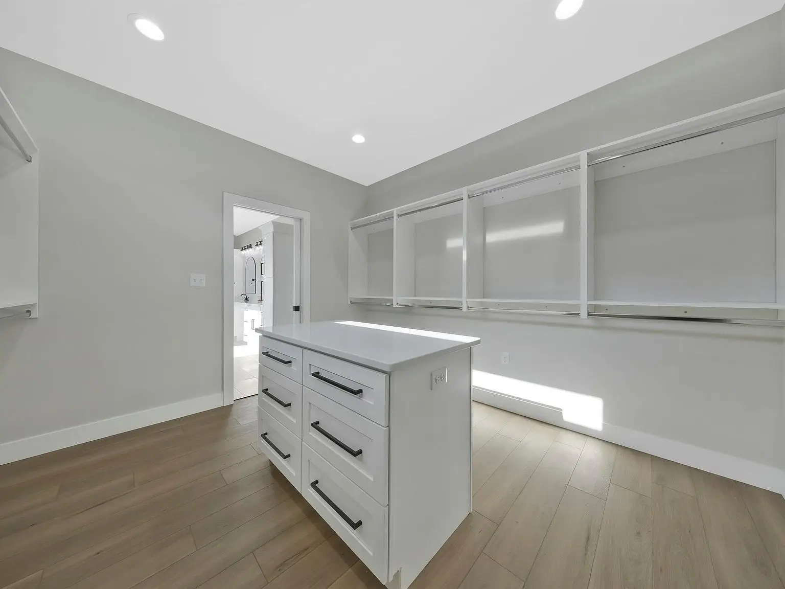 Spacious walk-in closet in the Ava floor plan, with island, empty shelves, and wood flooring.