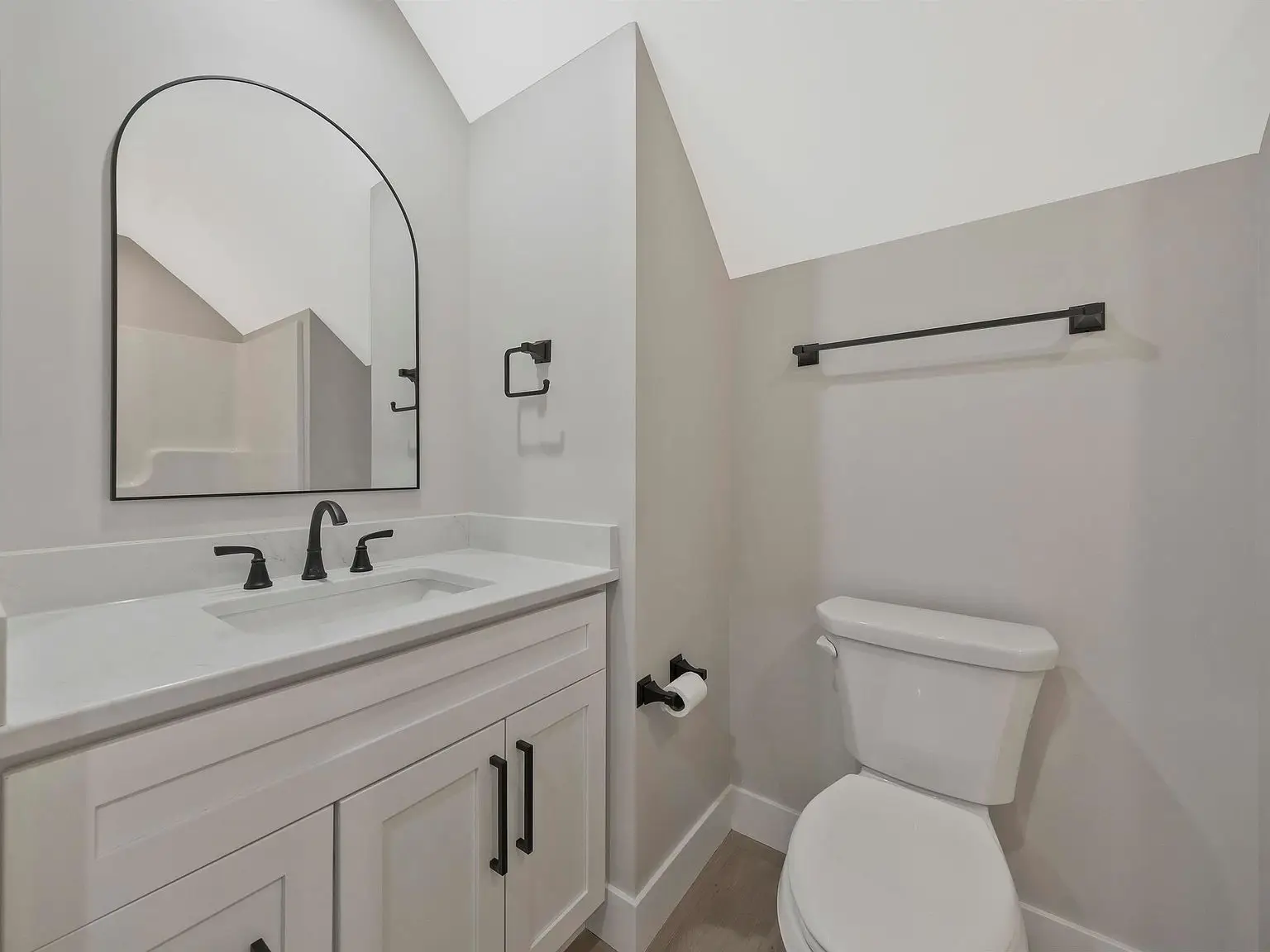 White bathroom with Ava floor plan features under a sloped ceiling, sink, towel rack, and toilet.