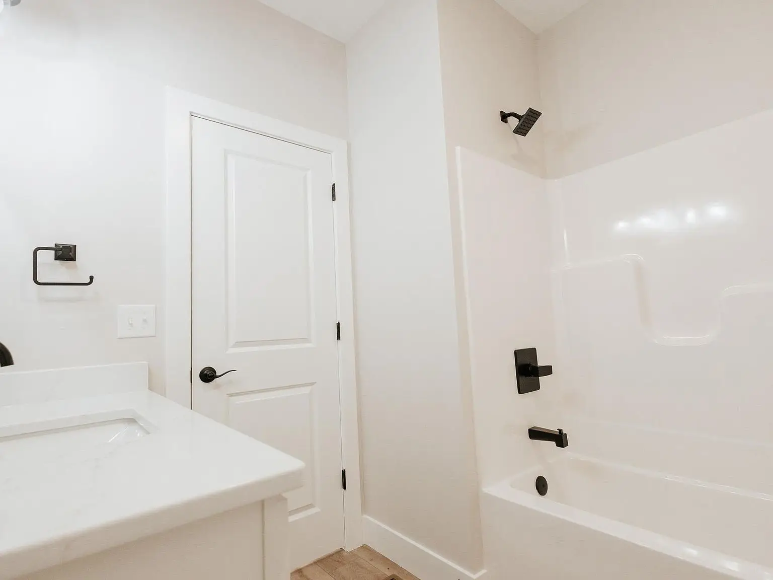 White bathroom with a bathtub, black fixtures, and sink in the Asher floor plan, door closed.