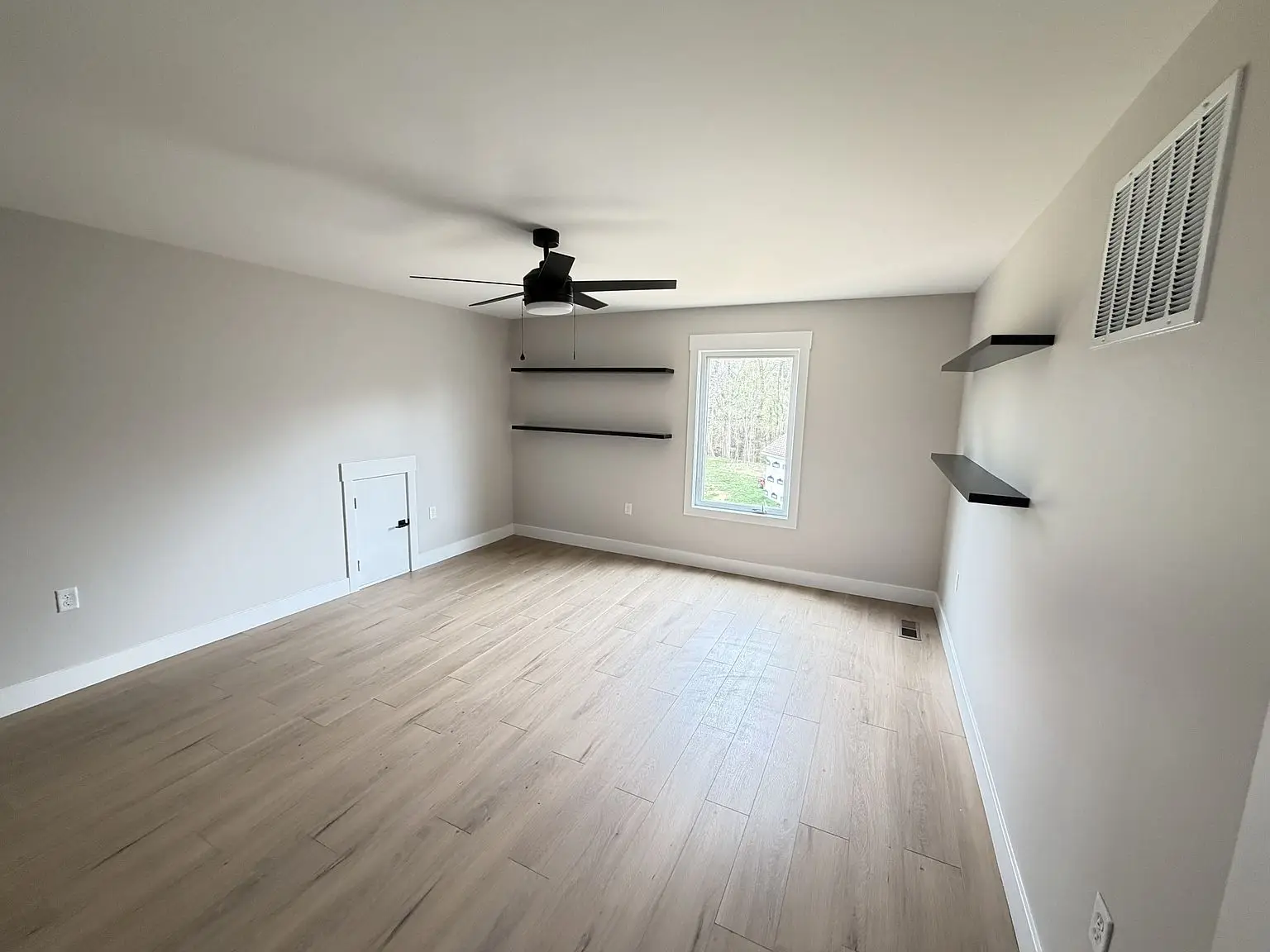 Empty room in Robin floor plan with light wood floor, white walls, and wall shelves.