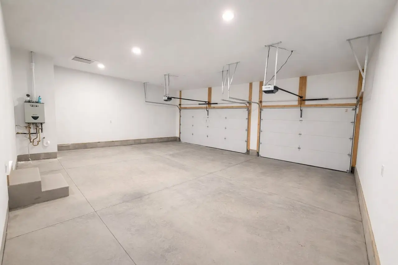 Spacious three-car garage in the Asher floor plan with white walls, concrete floor, and lights.