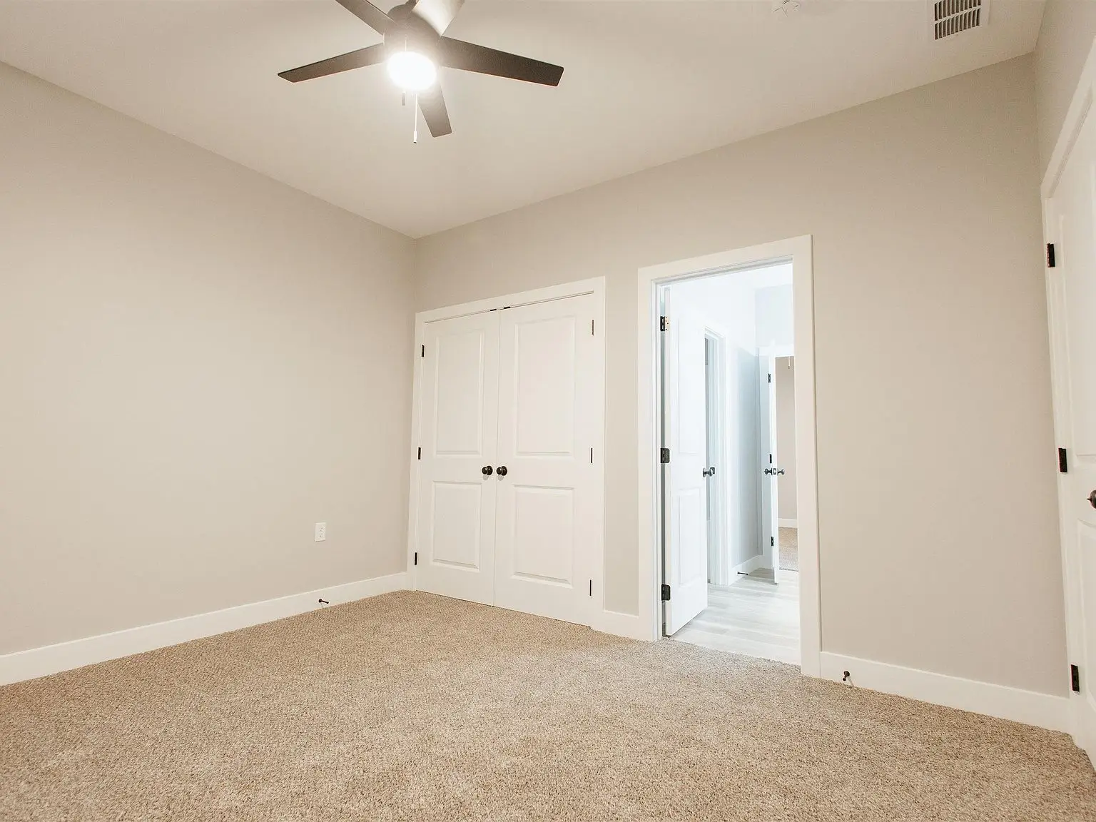 Empty beige carpeted room in the Eleanor home with white double closet doors and ceiling fan.