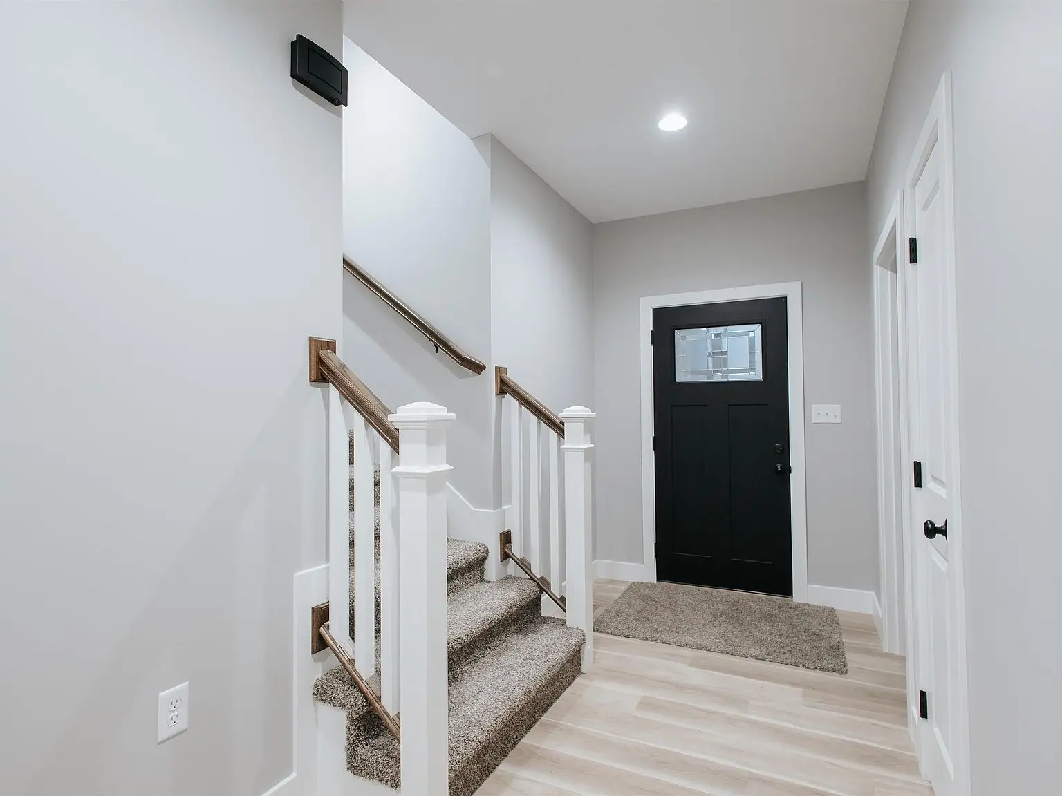 A small entryway with a black door, beige stairs, light wood floors, in the Eleanor floor plan.
