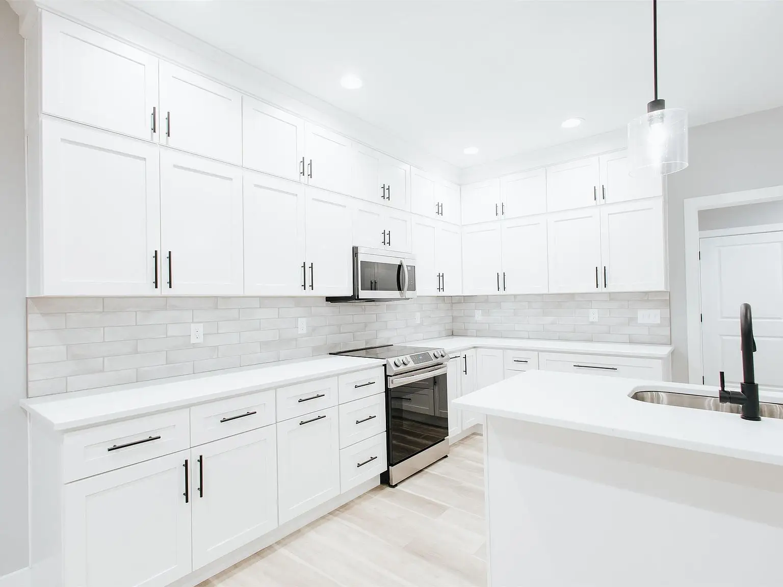 Modern kitchen in the Eleanor floor plan with white cabinets and a black faucet on the island.