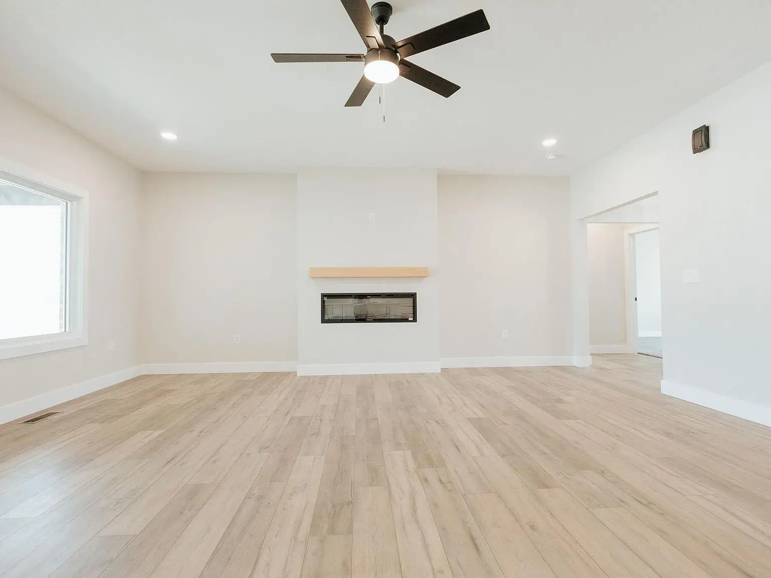 Empty living room with light wood floors, Asher floor plan, fireplace, and ceiling fan.
