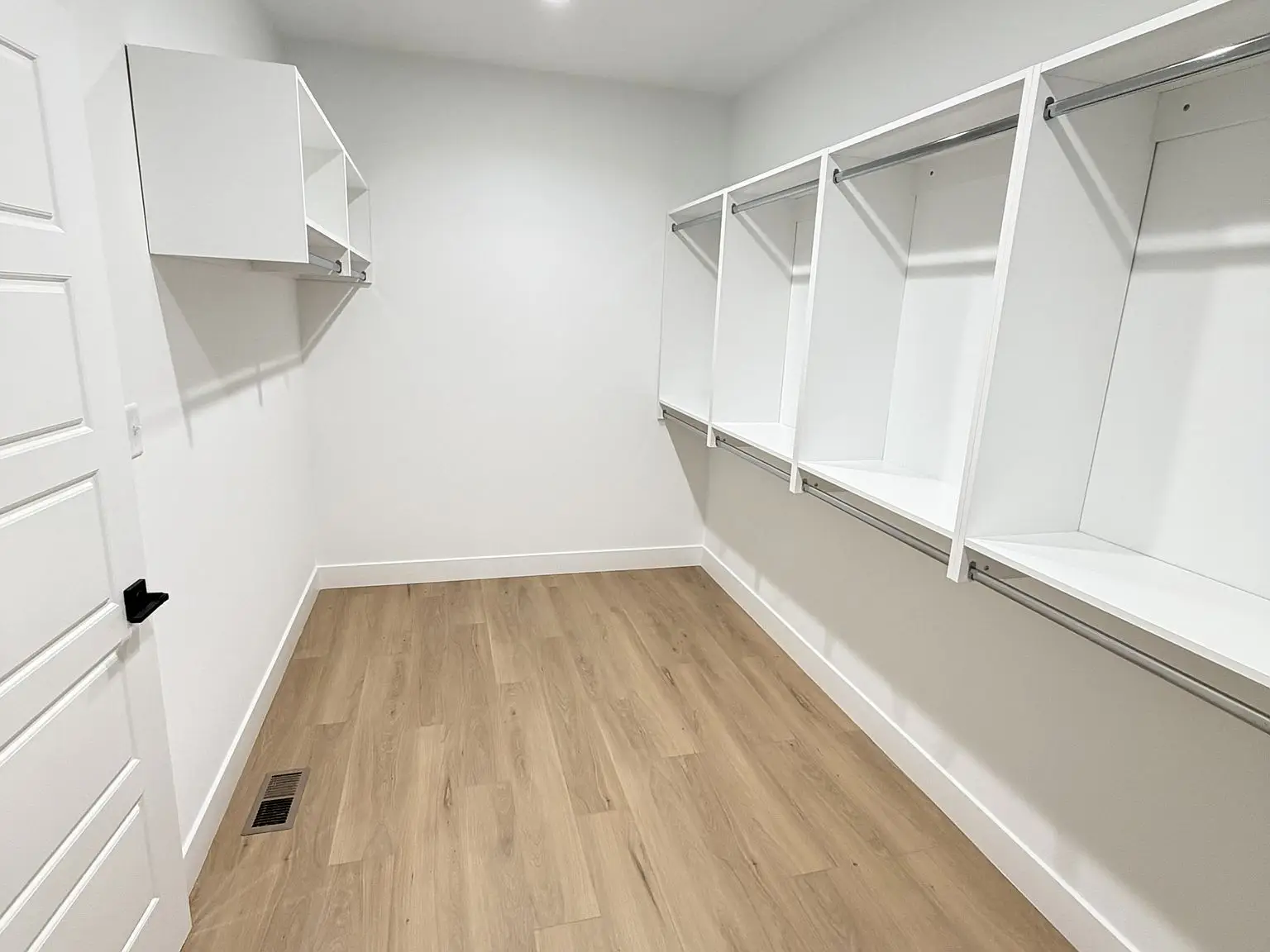 Empty walk-in closet with white shelves, rods, light wood flooring in the Robin floor plan.