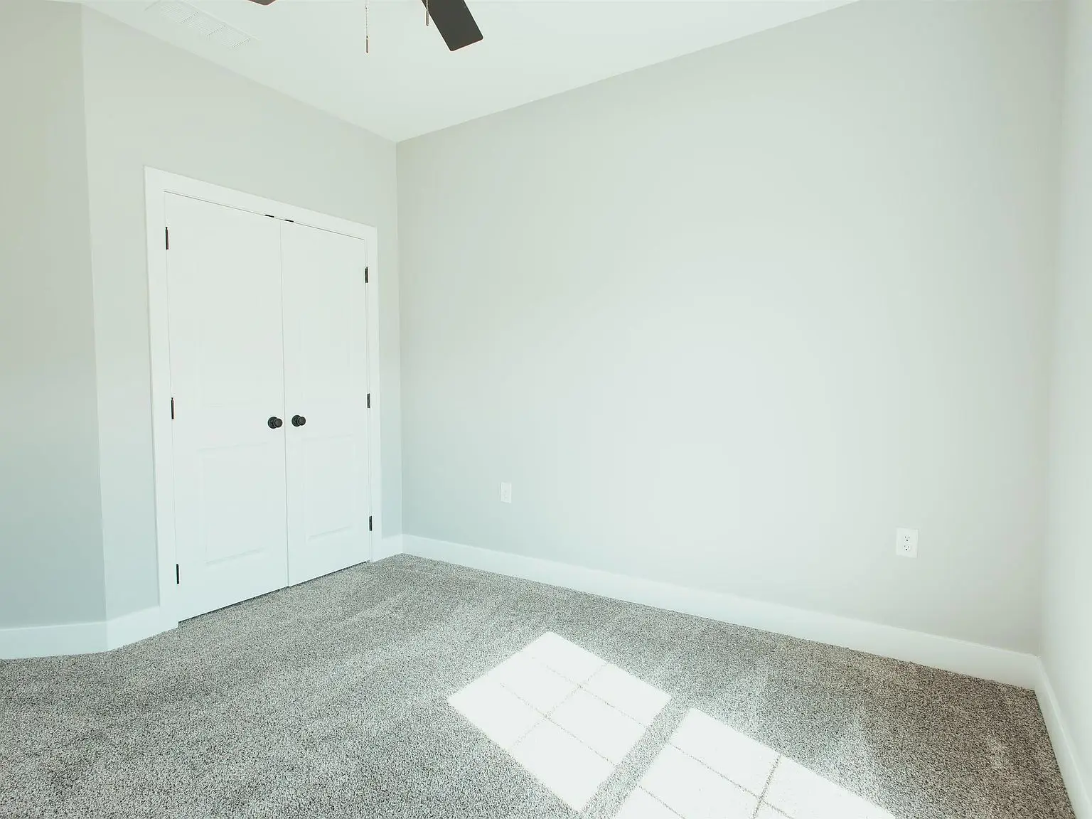 Empty room with gray carpet, white double doors, and Kirkwood floor plan sunlight on the floor.