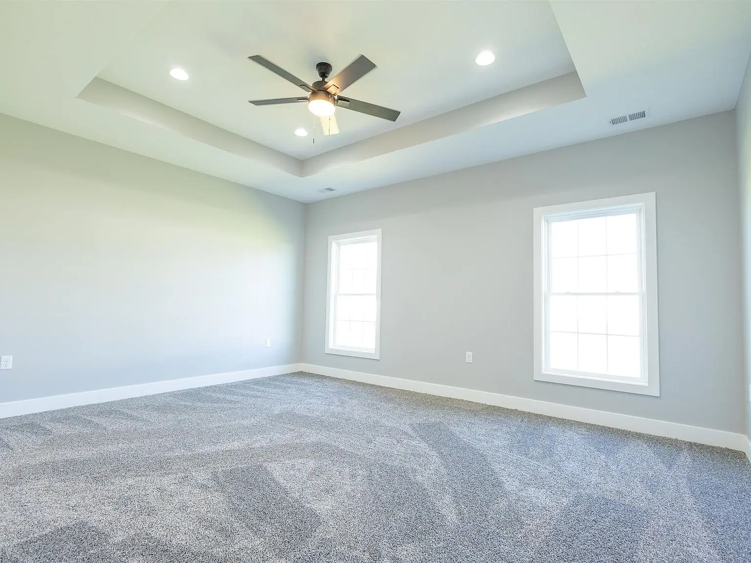 Empty room with gray carpet, Kirkwood floor plan, two windows, ceiling fan, and light gray walls.