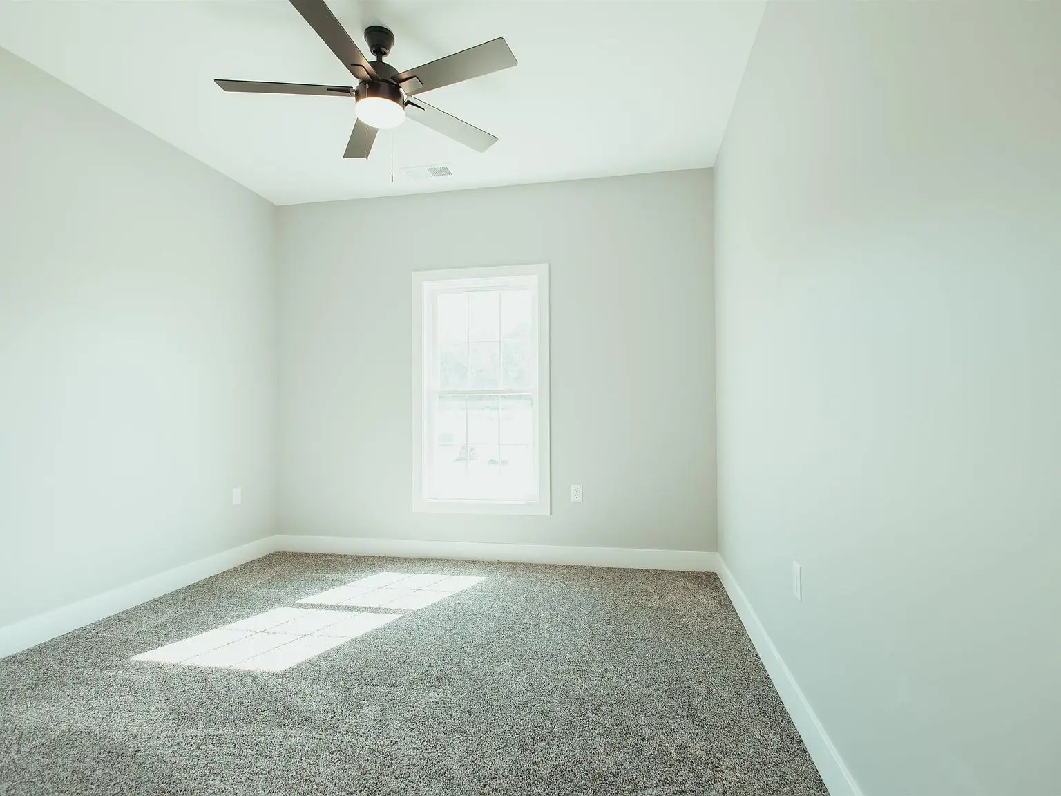 Empty Kirkwood floor plan with gray carpet, white walls, window, and ceiling fan with light.