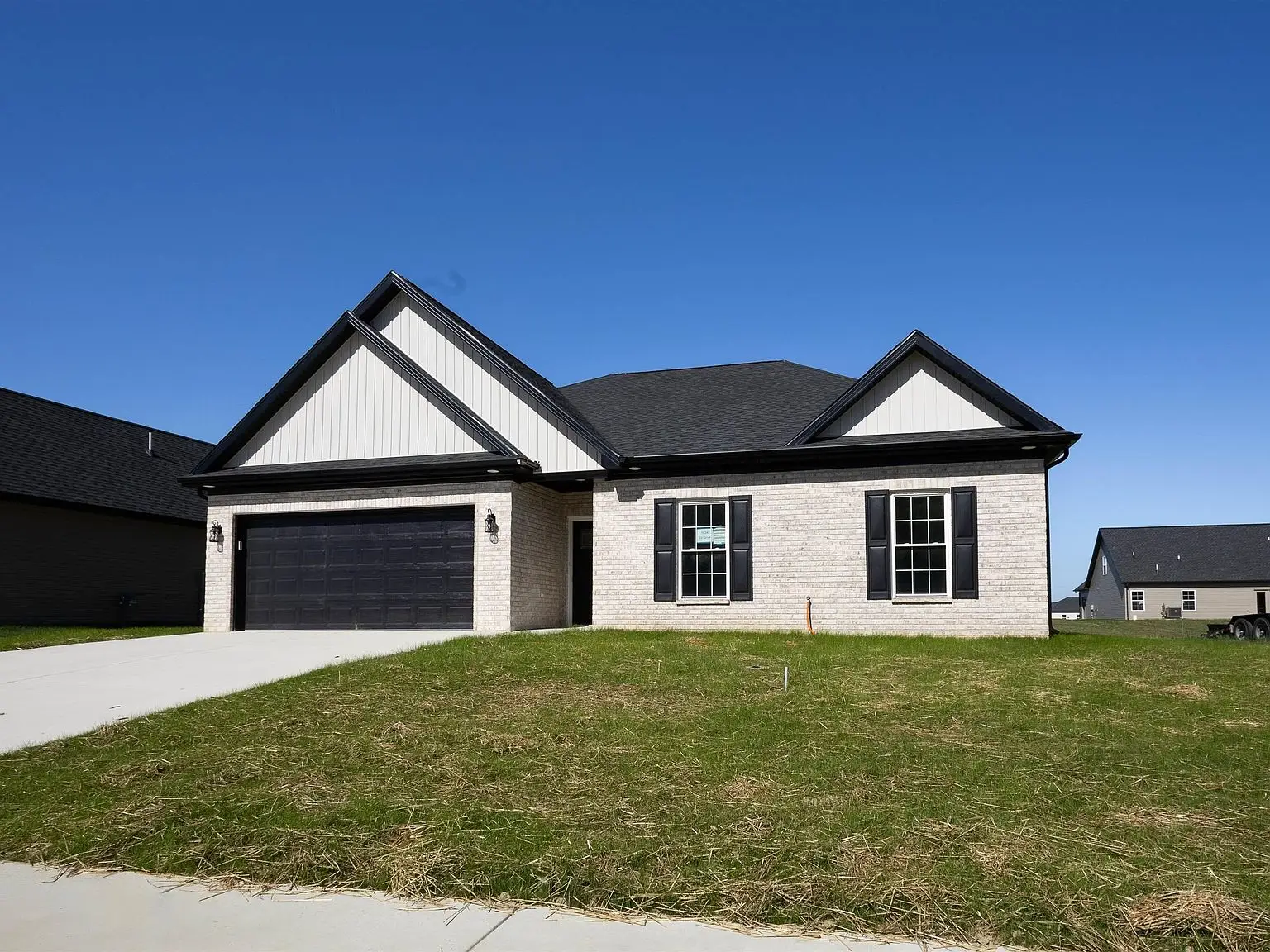 Single-story brick Kirkwood home with black roof, garage, and front lawn under a clear blue sky.