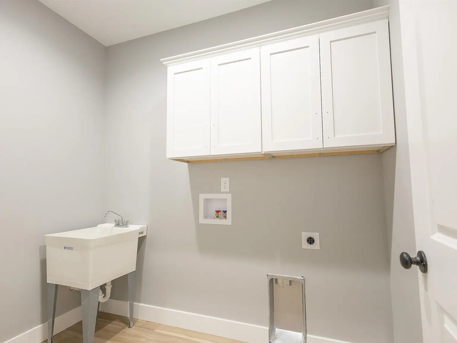 Laundry room in Chris Brown Homes 1624 Eli Dr with utility sink, white cabinets, gray walls.