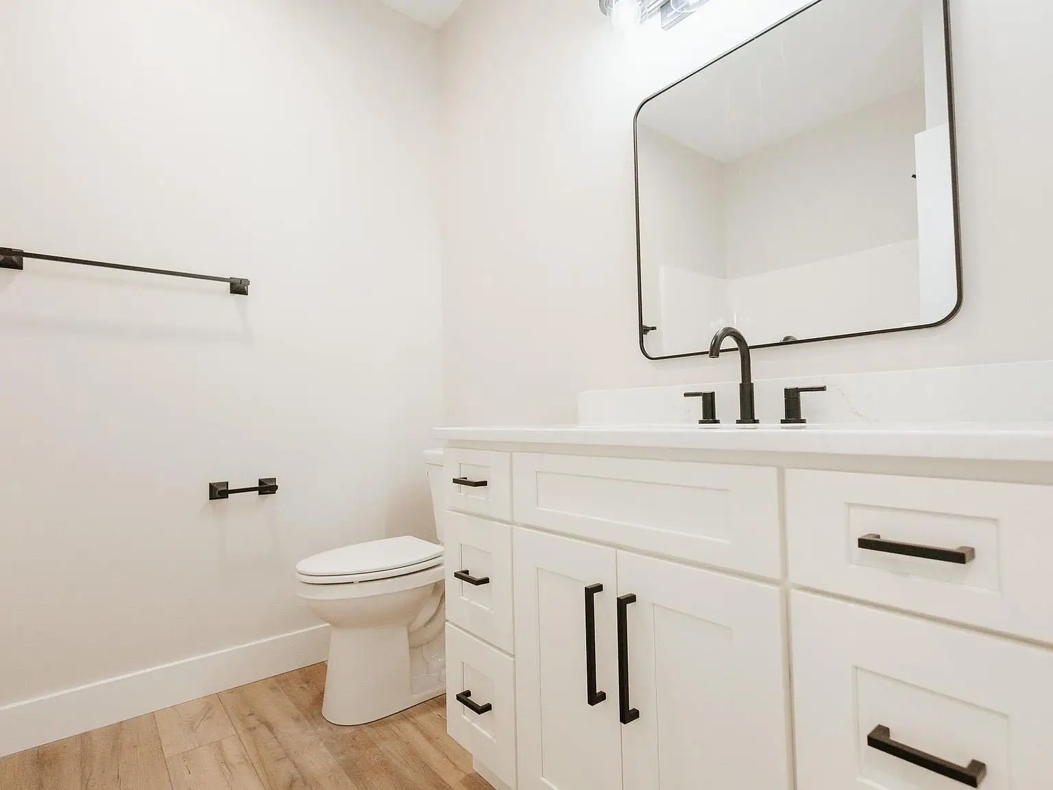 Modern bathroom with Asher floor plan, white vanity, black fixtures, and wood-style flooring.