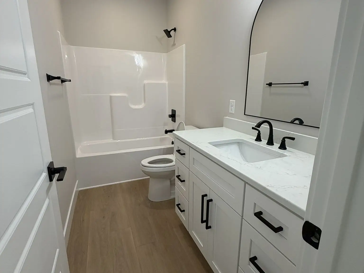 Modern bathroom in the Robin floor plan with white tub, black fixtures, and wood flooring.