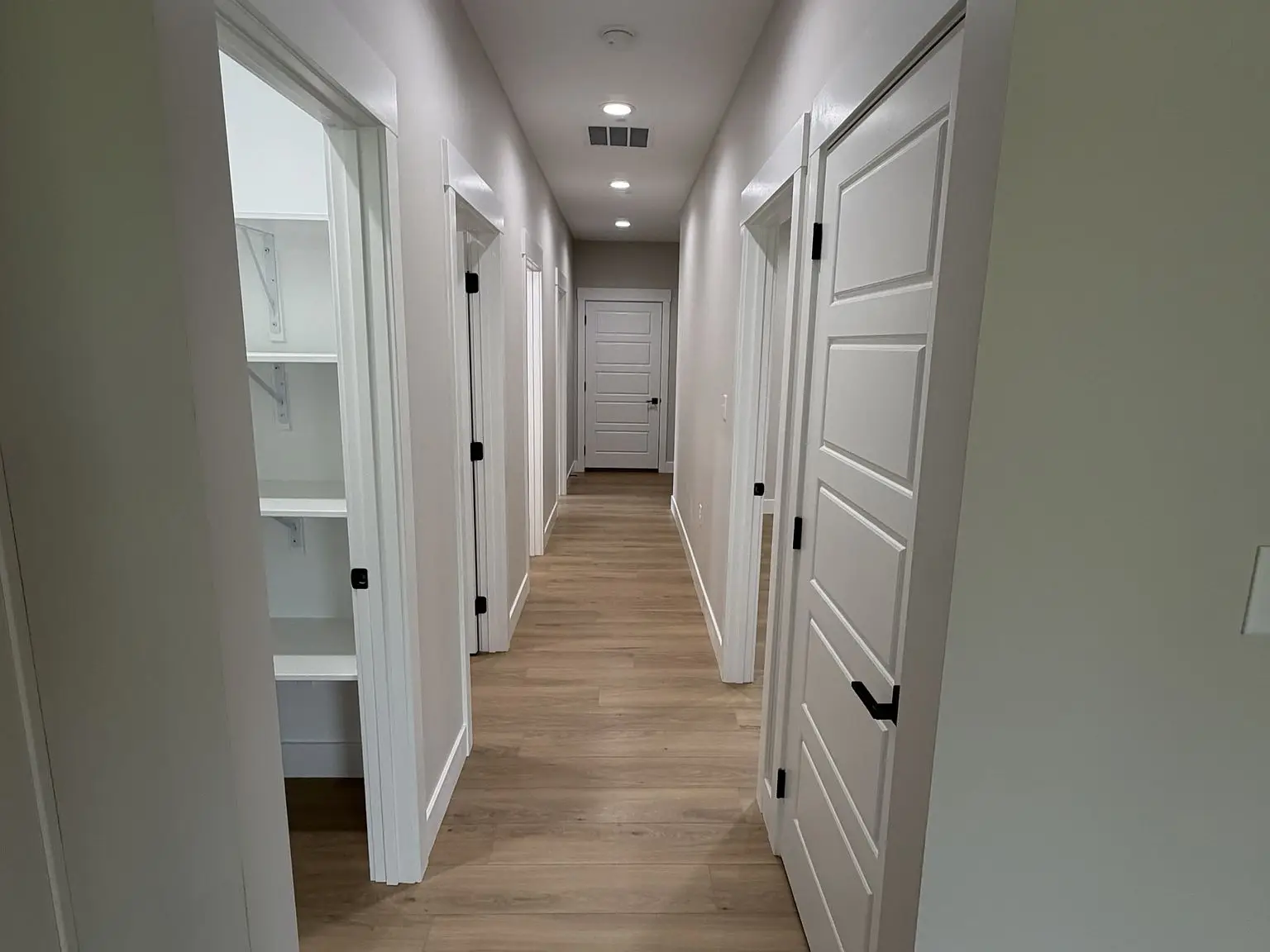 A hallway with wooden floors, white doors, and shelves—part of the Robin floor plan design.