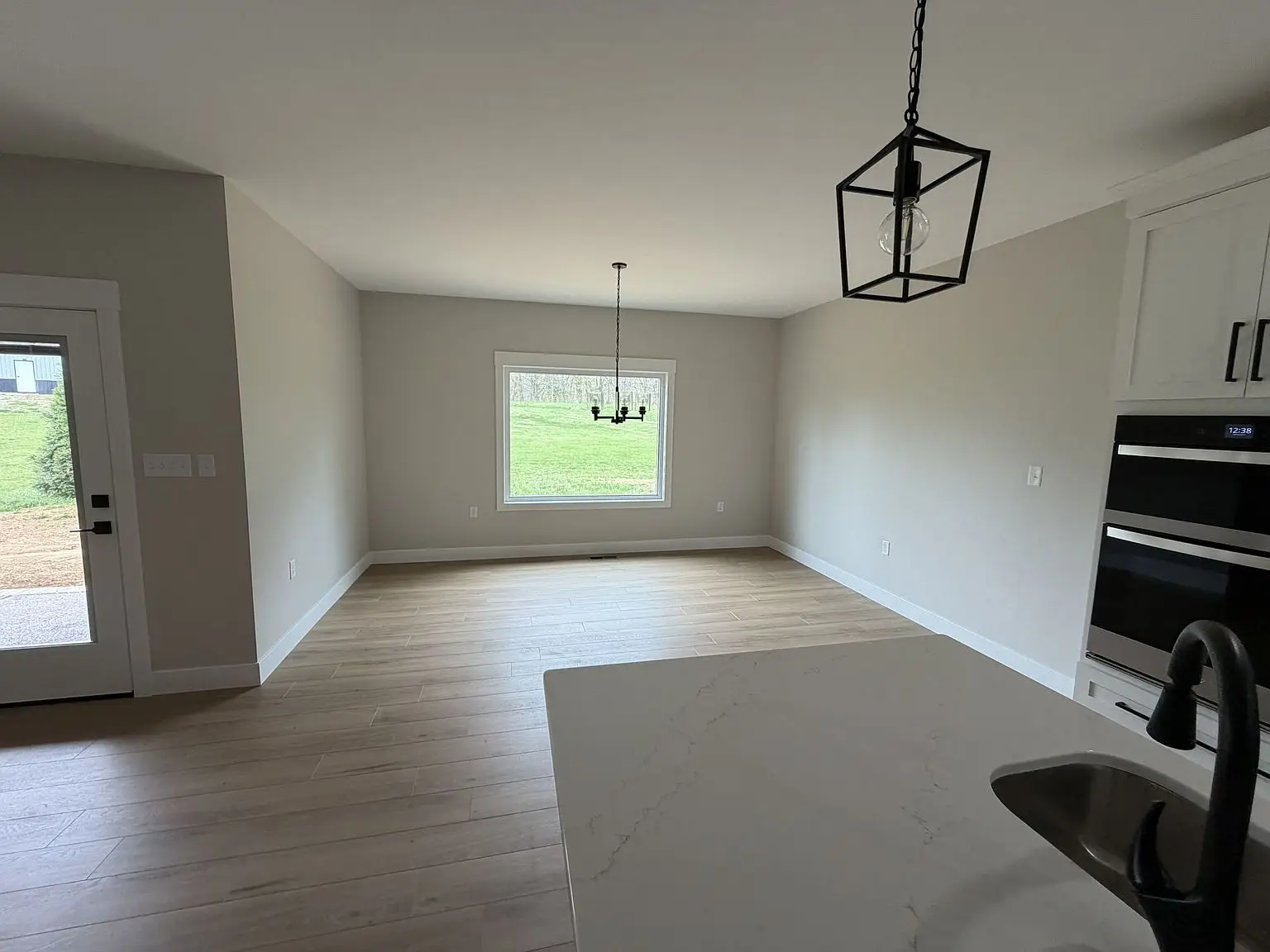 Empty room with light wood floor, large window, and chandelier in Chris Brown Homes’ Robin plan.