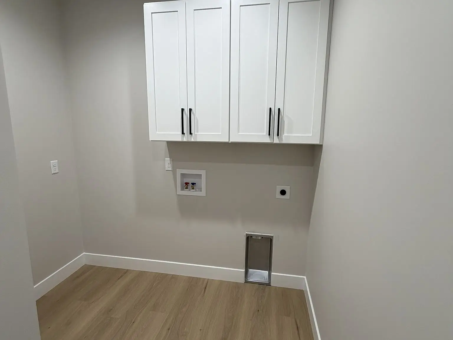 Empty laundry room in Chris Brown Homes’ Robin floor plan with white cabinets and wood floor.