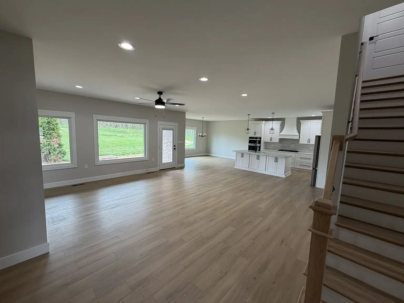 Open living area with wood floors, Robin floor plan kitchen, large windows, and right staircase.