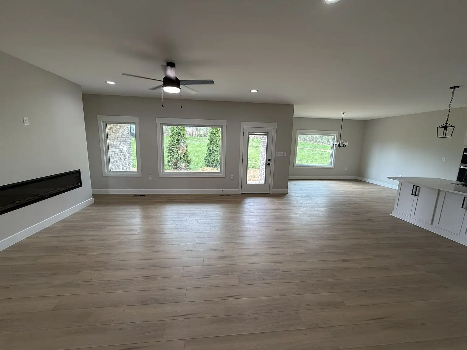 Spacious empty room in Robin floor plan with wood floor, large windows, and modern fixtures.