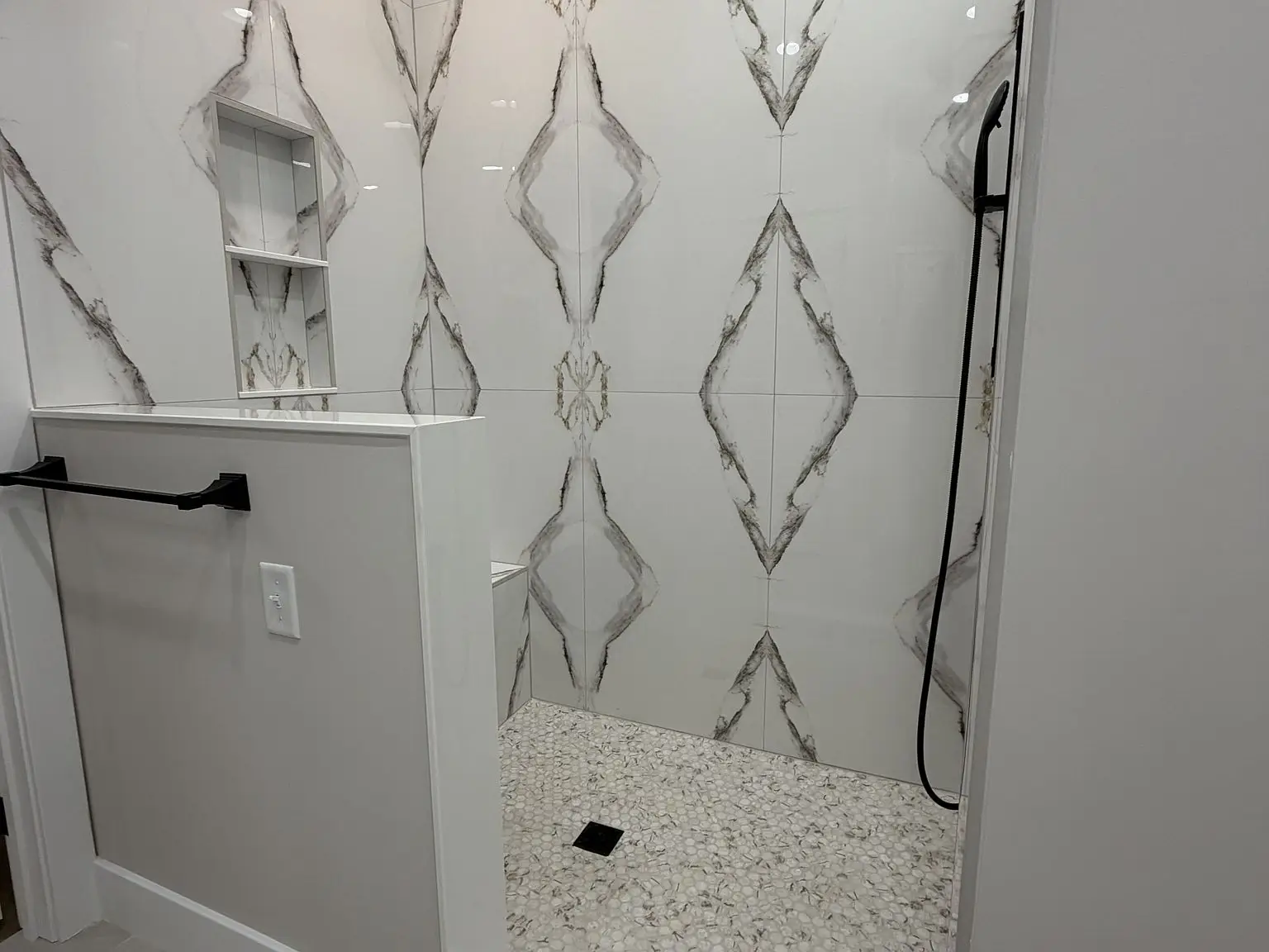 Walk-in shower: patterned tile wall, Robin floor plan, built-in shelf, pebble floor.