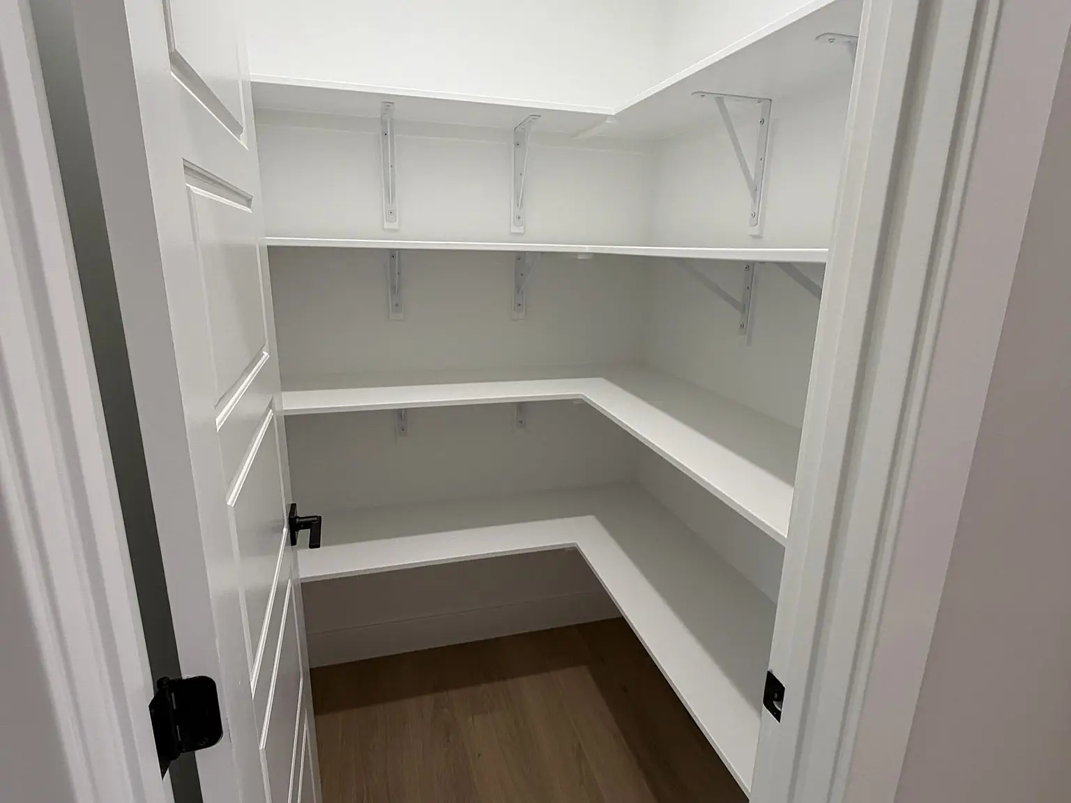 White, empty walk-in pantry with three shelves and Robin floor plan light wood flooring.
