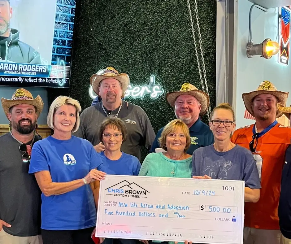 Eight people, some in cowboy hats, hold a $500 donation check, giving back to community indoors.