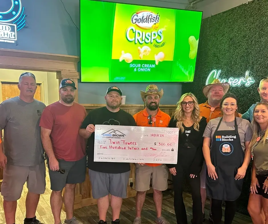 Ten people giving back to community hold a $500 check in a restaurant under a Goldfish ad.