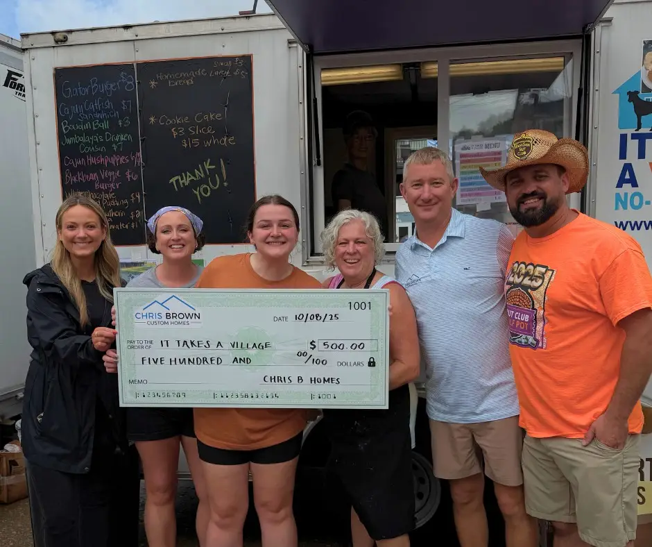 Six people stand together, giving back to community while holding a $500 check by a food truck.
