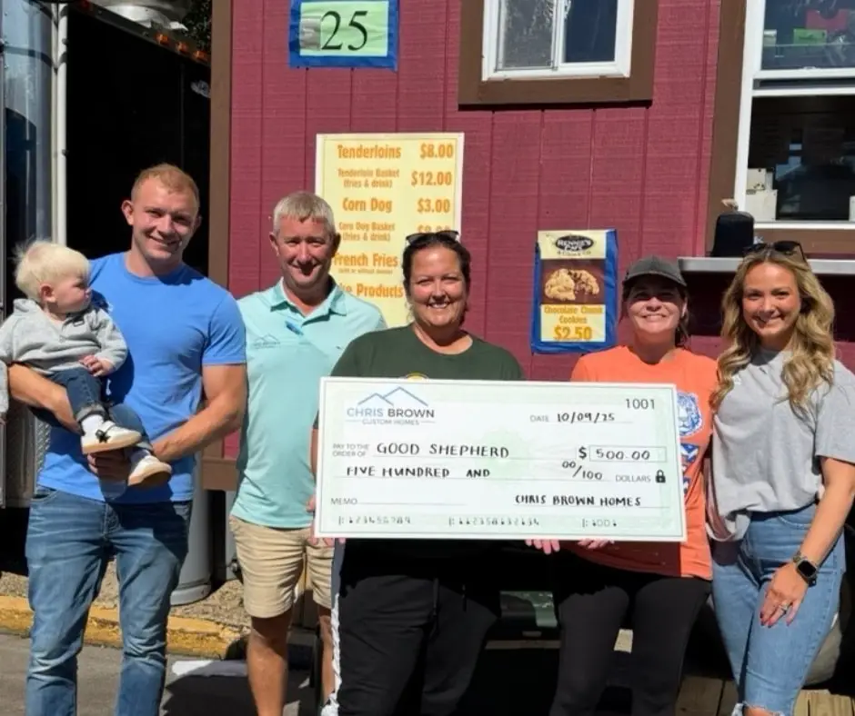 Six adults and a child hold a $500 check outside a food stand, giving back to community.
