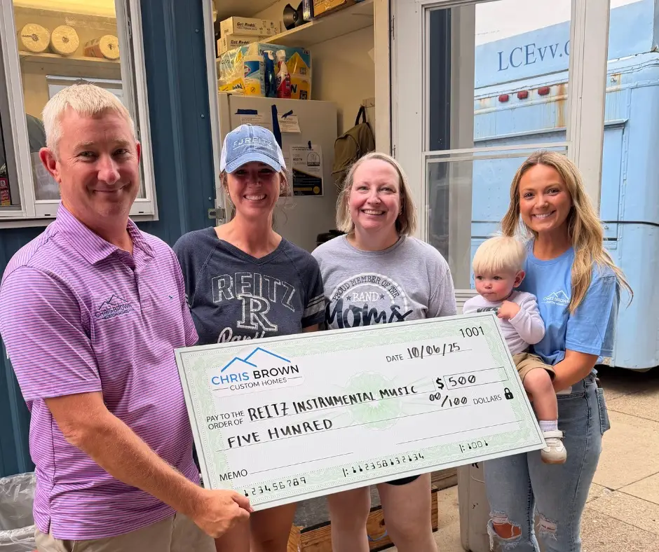 Four adults and a child smile with a $500 check, giving back to community outside a building.