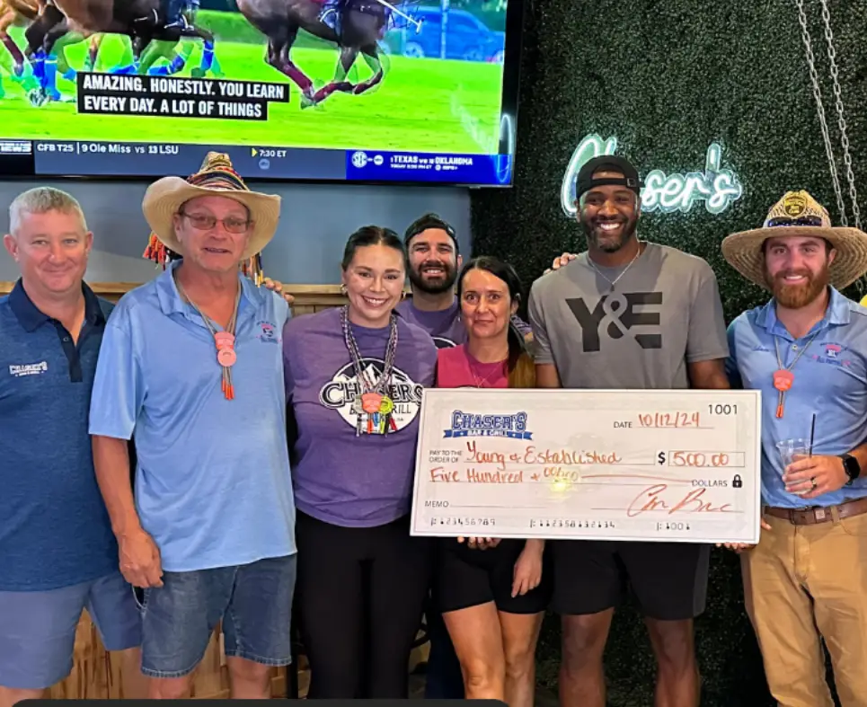 Six people pose indoors, one holds a large $500 check labeled Young Ex Scholarship..