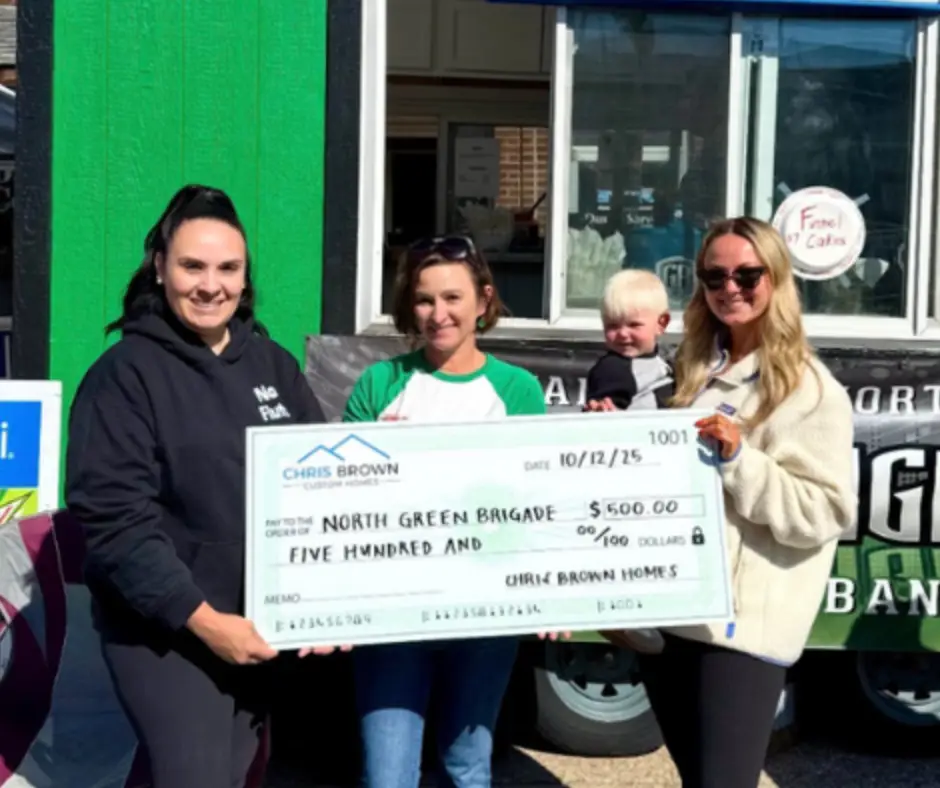 Four women and a child hold a large check for $500 from Chris Brown Homes at an outdoor event.