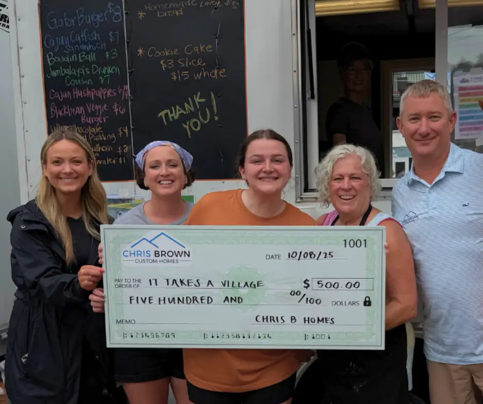 Five people smiling and holding a large check for $500 in front of a food truck.