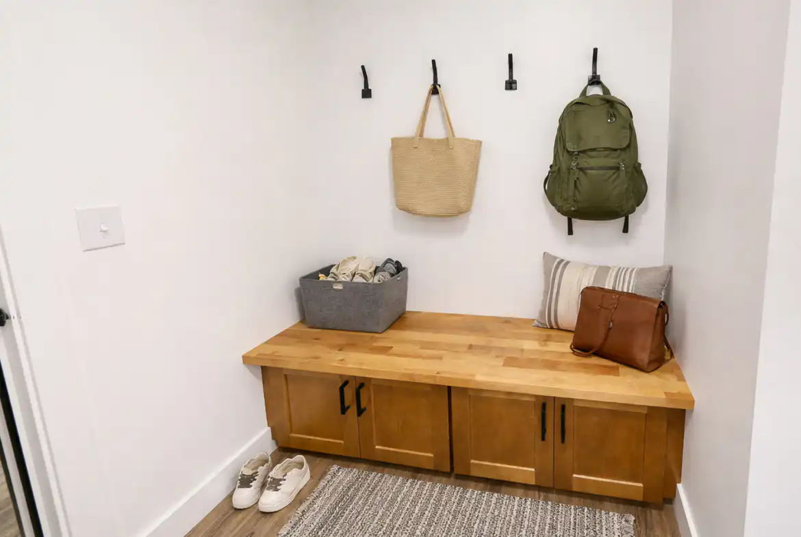 Leo mudroom storage bench with wood cabinets, black hooks, bags, shoe bin, and striped pillow.